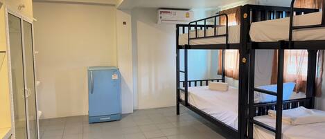 A dormitory room with bunk beds, a refrigerator, and a window with curtains.