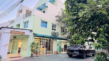 A two-story building with a green facade, a car parked in front, and a tree to the right.
