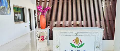 A reception area with a white console table labeled "BUPATARA," a small white side table with pink flowers, and a vertical wooden slat backdrop.