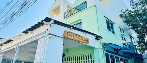 A two-story building with a green and white facade, a signboard, and a gated entrance.