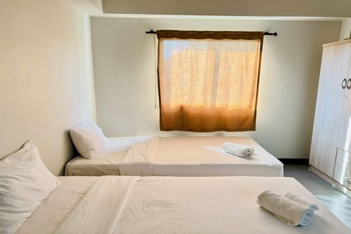 Habitación de hotel con dos camas, un armario y una ventana con cortinas.