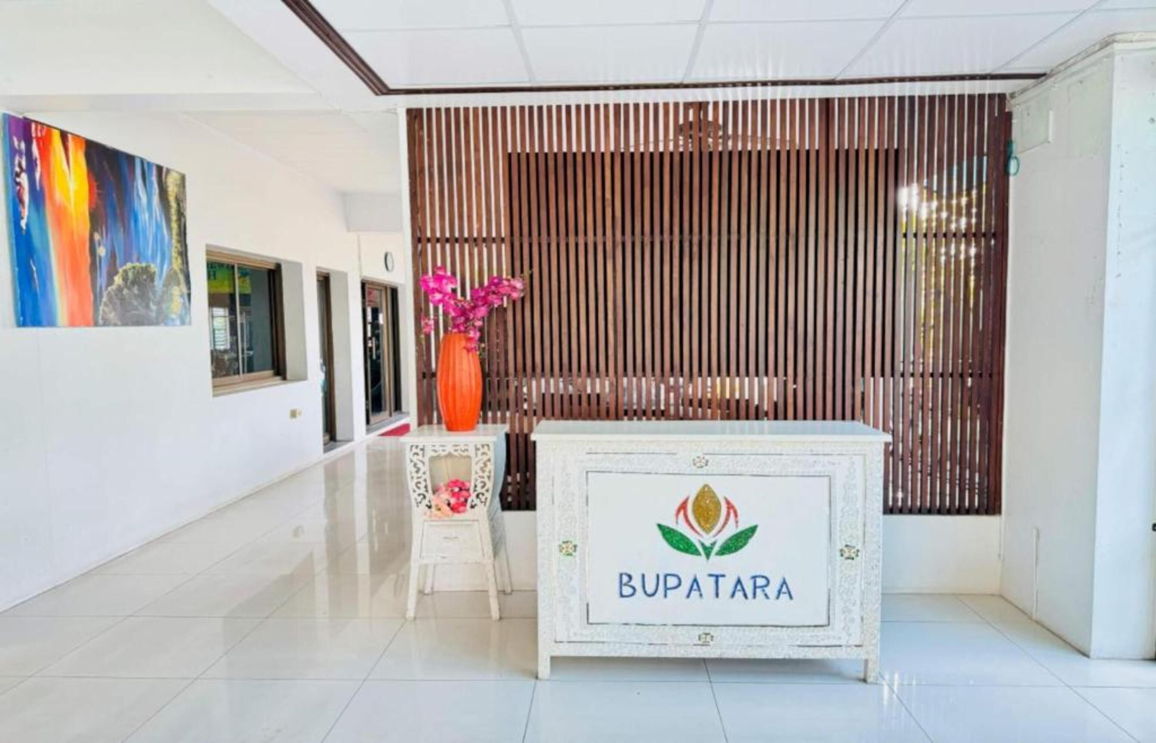 A reception desk with a logo, a decorative vase with flowers, a small table with a floral arrangement, and a colorful painting on the wall.