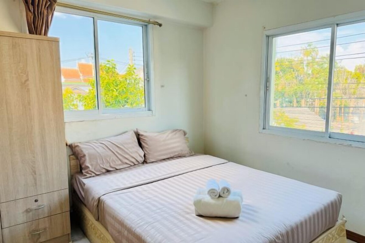 Un dormitorio con cama, armario de madera y dos ventanas con vistas al verdor.
