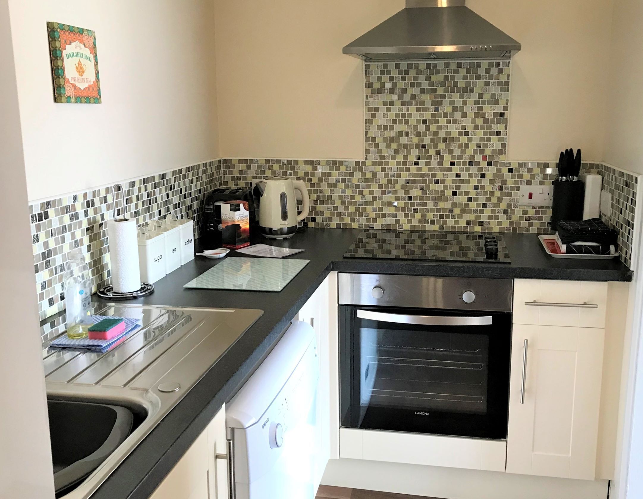 A kitchen with a black countertop, a stainless steel range hood, a coffee maker, and a microwave.