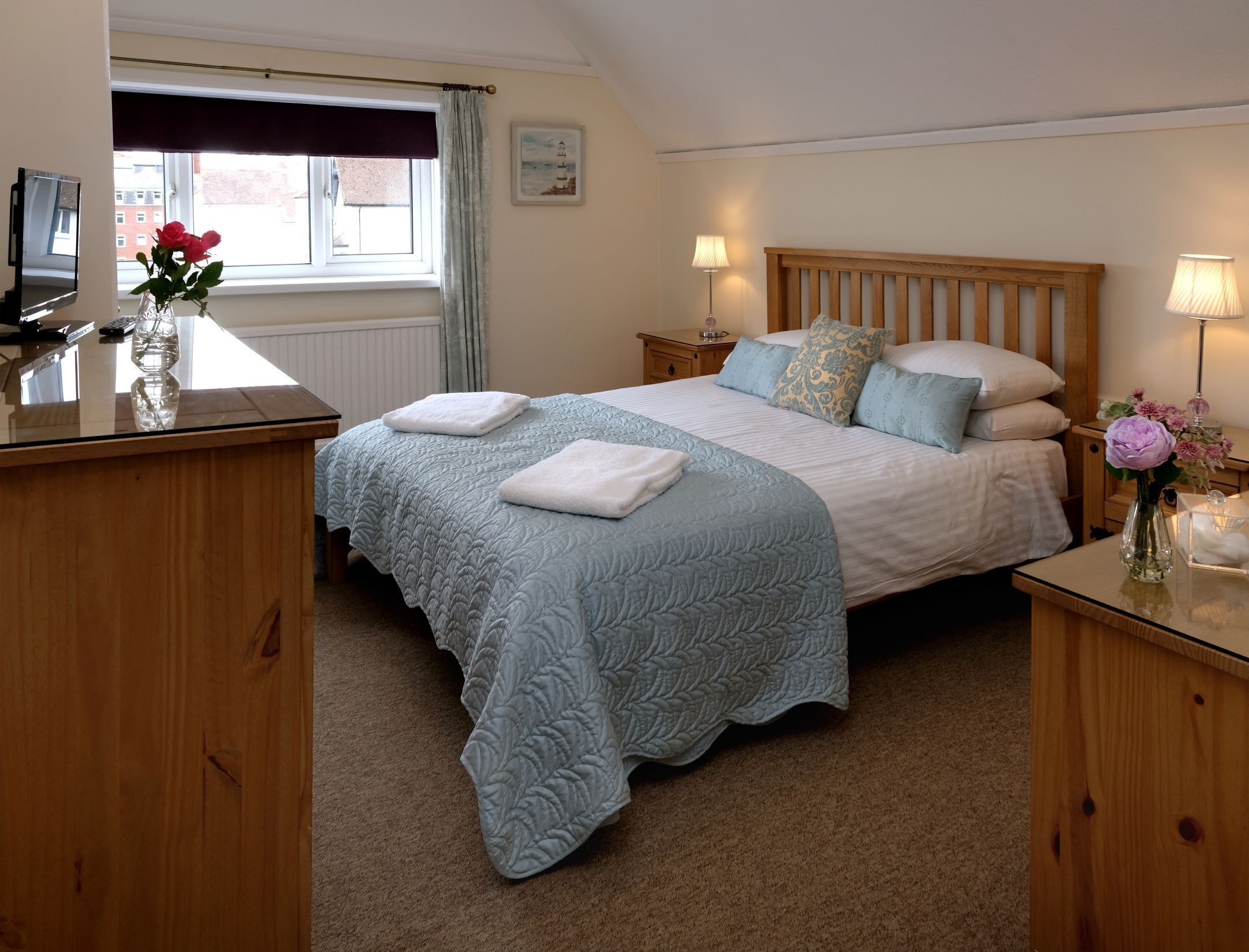 A bedroom with a large bed, two bedside tables, a desk, a window with curtains, and a lamp.