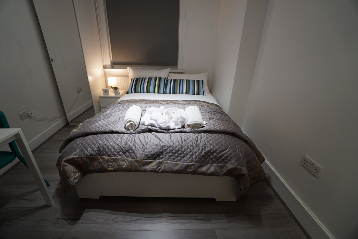 Una cama bien hecha con un cojín a rayas, una mesita de noche con una lámpara y una silla.