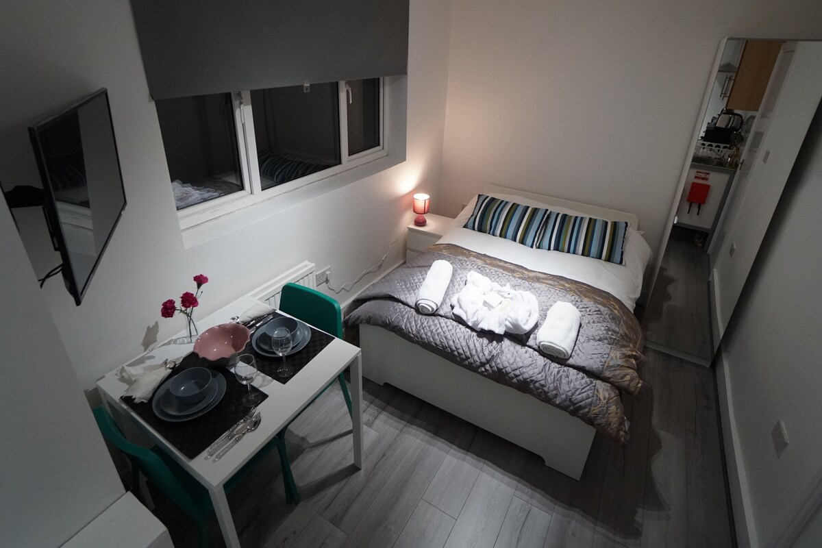 Una habitación de hotel compacta con una cama, una mesita de noche y un pequeño escritorio con una silla.
