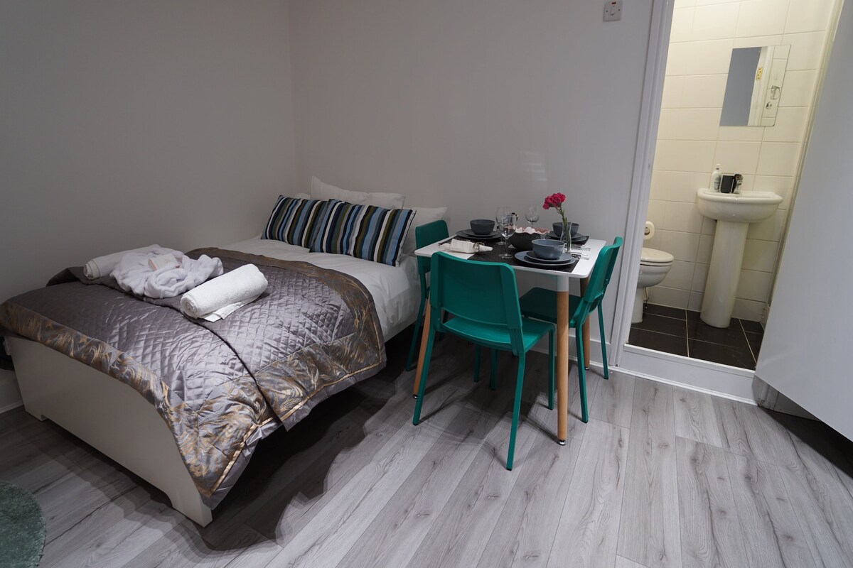 Se ve un dormitorio con cama, escritorio y baño a través de una puerta abierta.