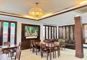 A spacious living area with a wooden dining table, sofas, and a large TV screen.