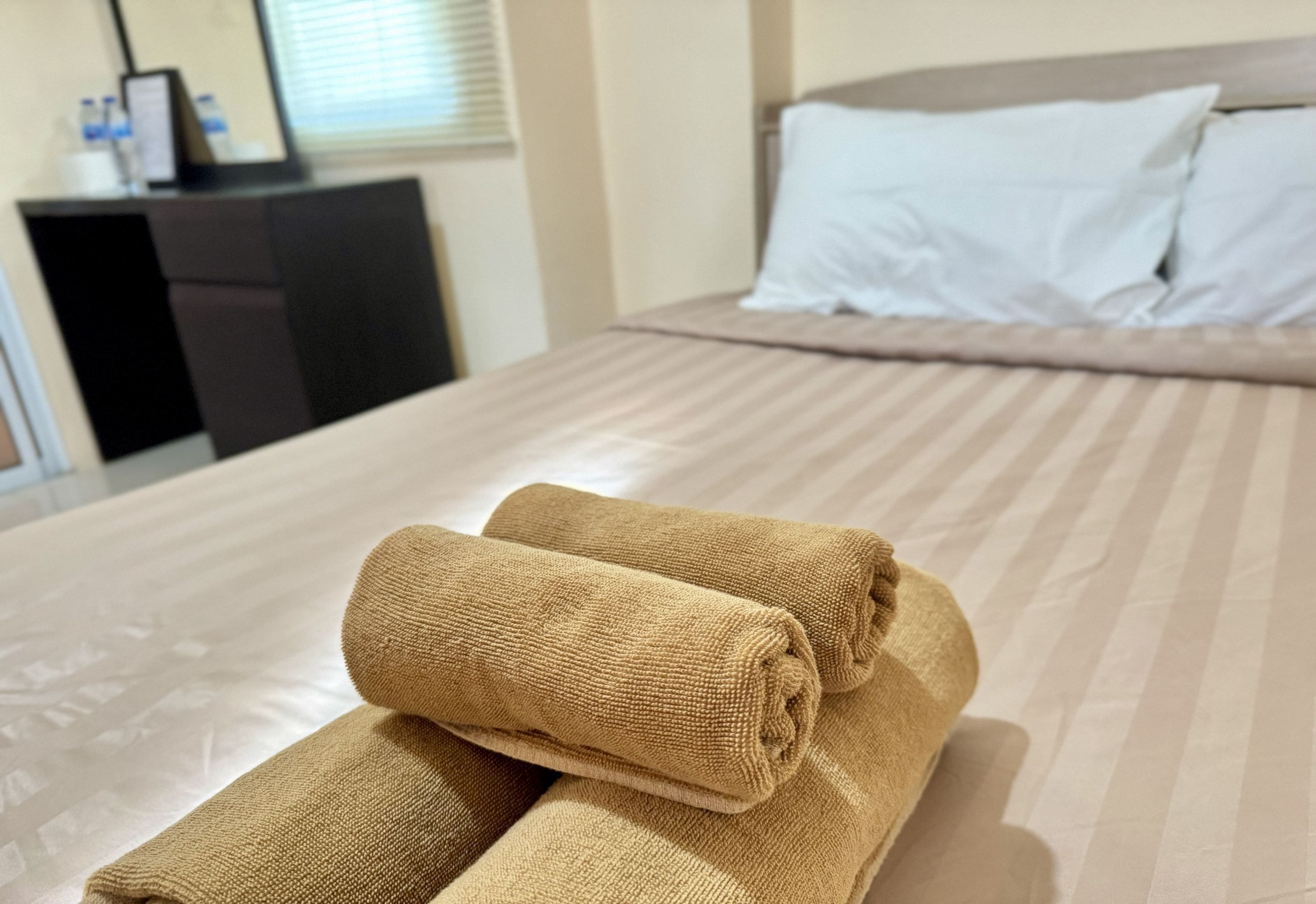 Una cama bien hecha con una colcha a rayas y dos toallas enrolladas encima.