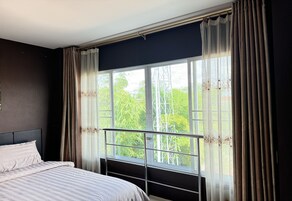 A bedroom with a large window, a bed, and curtains.