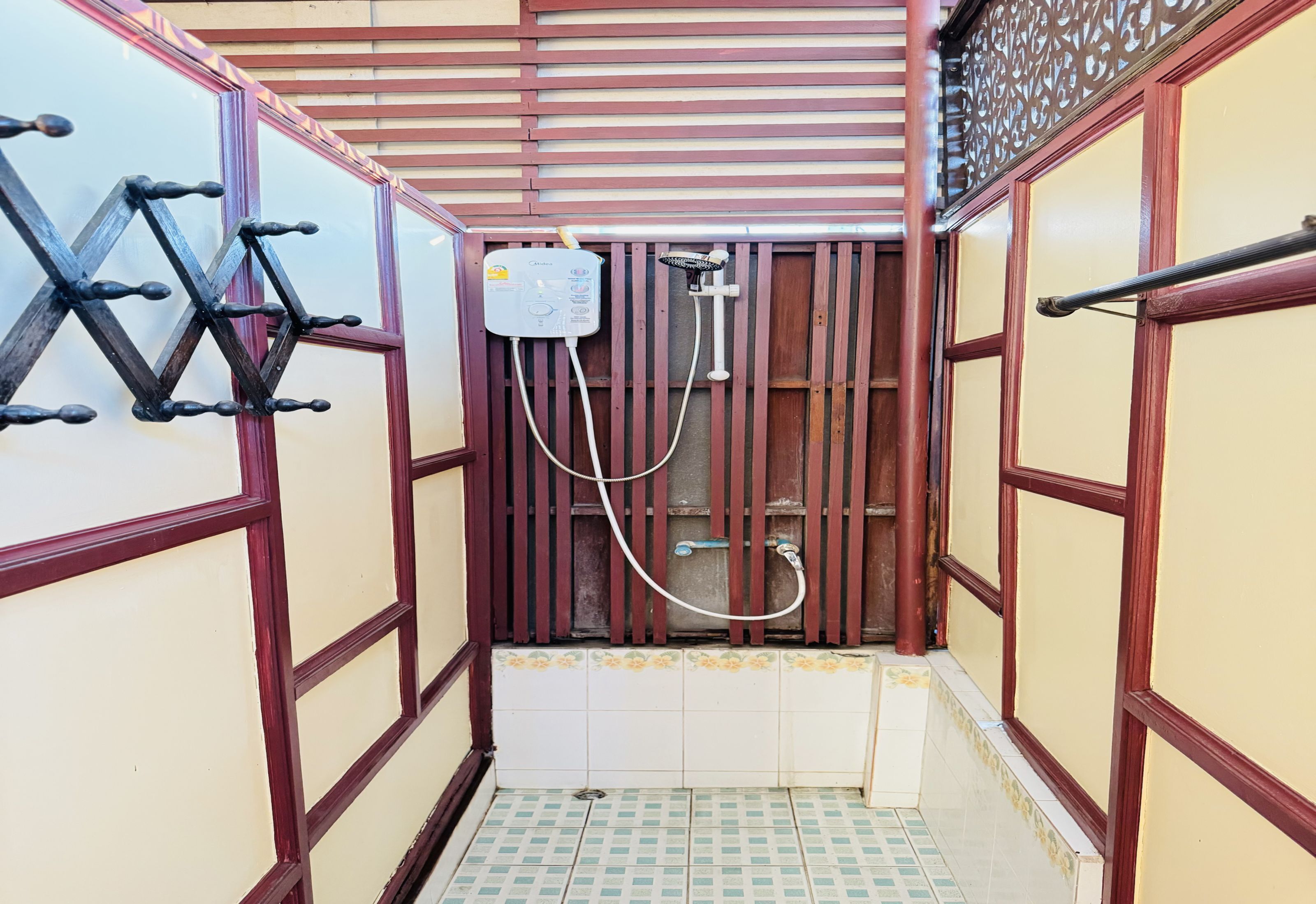 Un baño estrecho con ducha, suelo de baldosas y una celosía metálica decorativa en la pared.