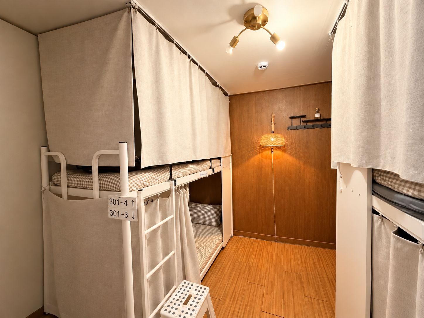 A compact room with bunk beds, a small stool, a wall-mounted shelf, and a ceiling light fixture.