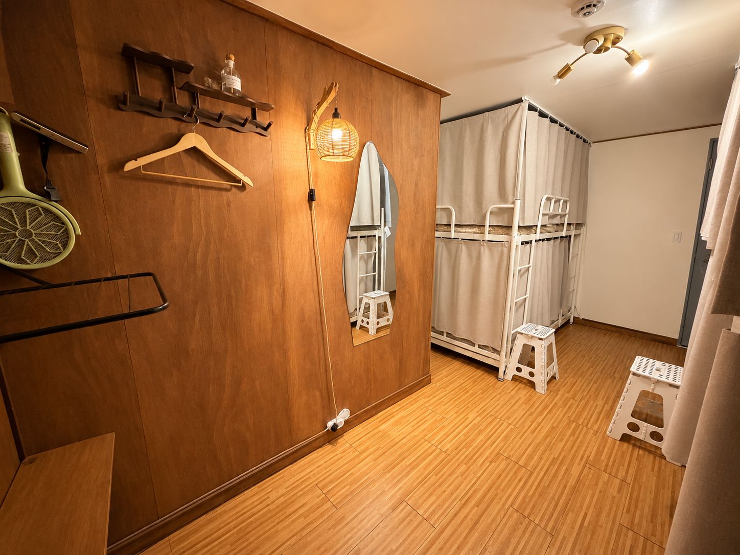 A room with wooden flooring, a wardrobe, a hanging light fixture, and a bed with a white headboard.