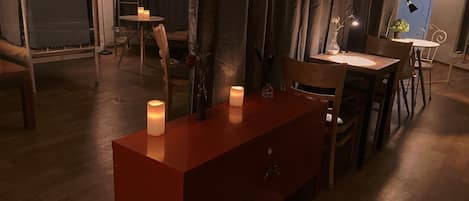 A dimly lit room with a wooden dining table, chairs, and a red cabinet with candles.