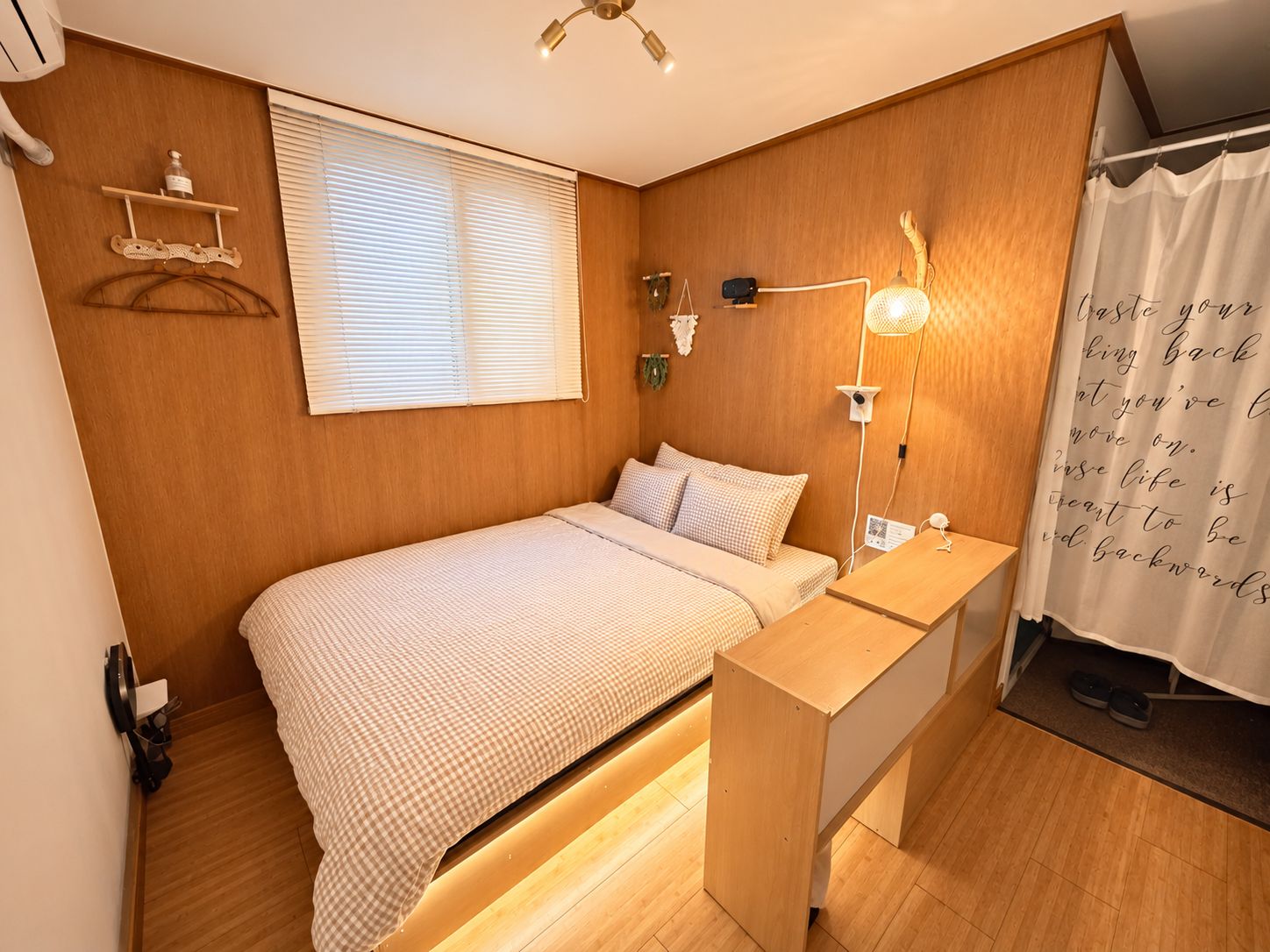 A bedroom with a bed, bedside table, lamp, and a wall-mounted shelf.