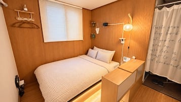 A bedroom with a bed, bedside table, lamp, and a wall-mounted shelf.