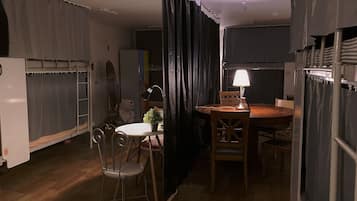 A compact room with a bunk bed, a dining table with chairs, a small potted plant, and a lamp.