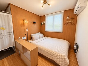 A compact bedroom with a single bed, a bedside table, a wall-mounted lamp, and a window with blinds.