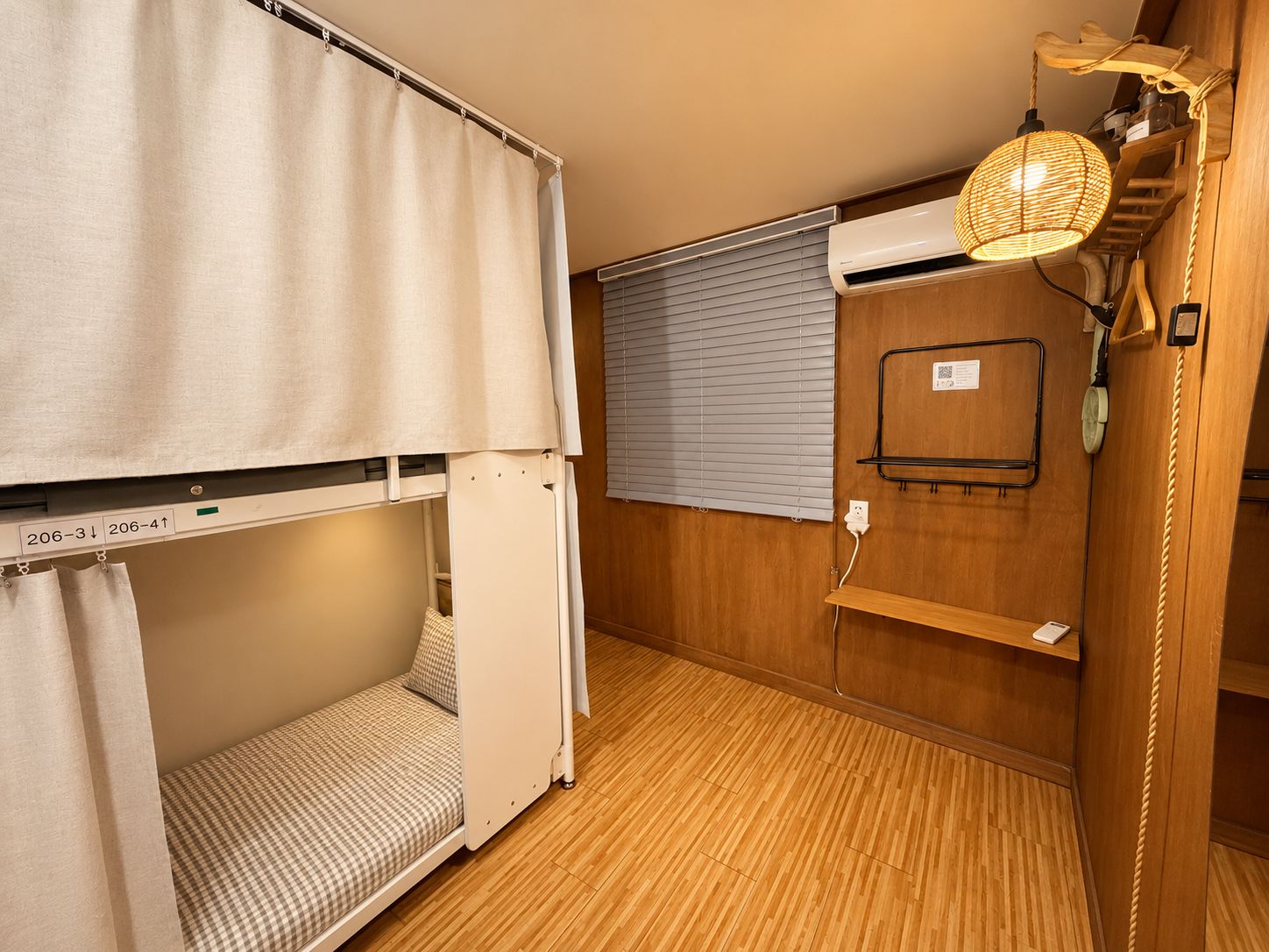Ein schlichter Raum mit Etagenbett, kleinem Tisch, Ablagefläche, fest installiertem Telefon und Fenster mit Jalousien.