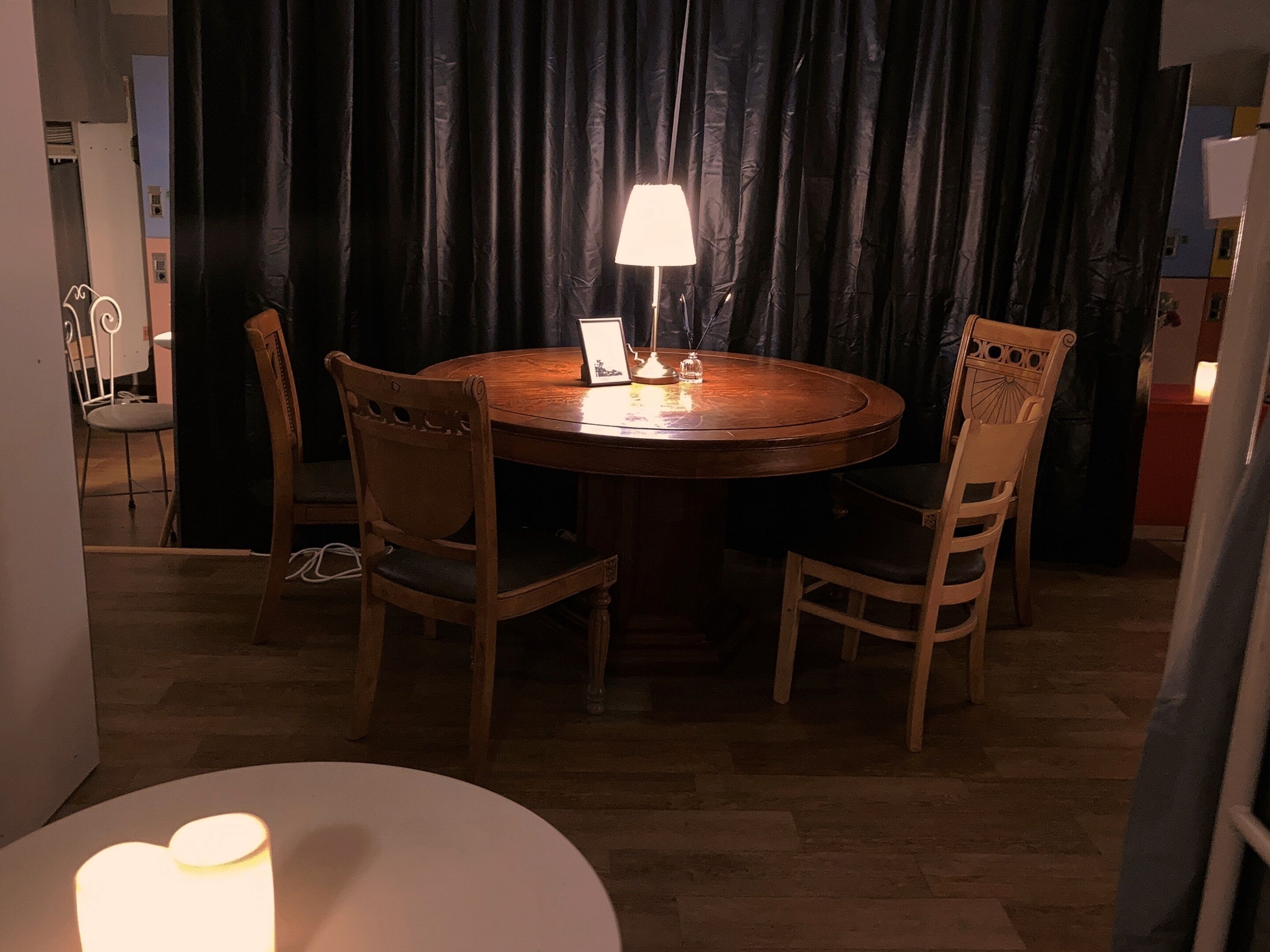 A round wooden dining table with a white table lamp, surrounded by four wooden chairs with cushioned seats.