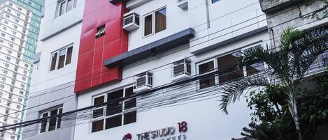 Ein mehrgeschossiges Gebäude mit einer auffälligen roten, vertikalen Streifung an der Fassade, Klimaanlagen und einem Schild, das "The Studio 18" zeigt.