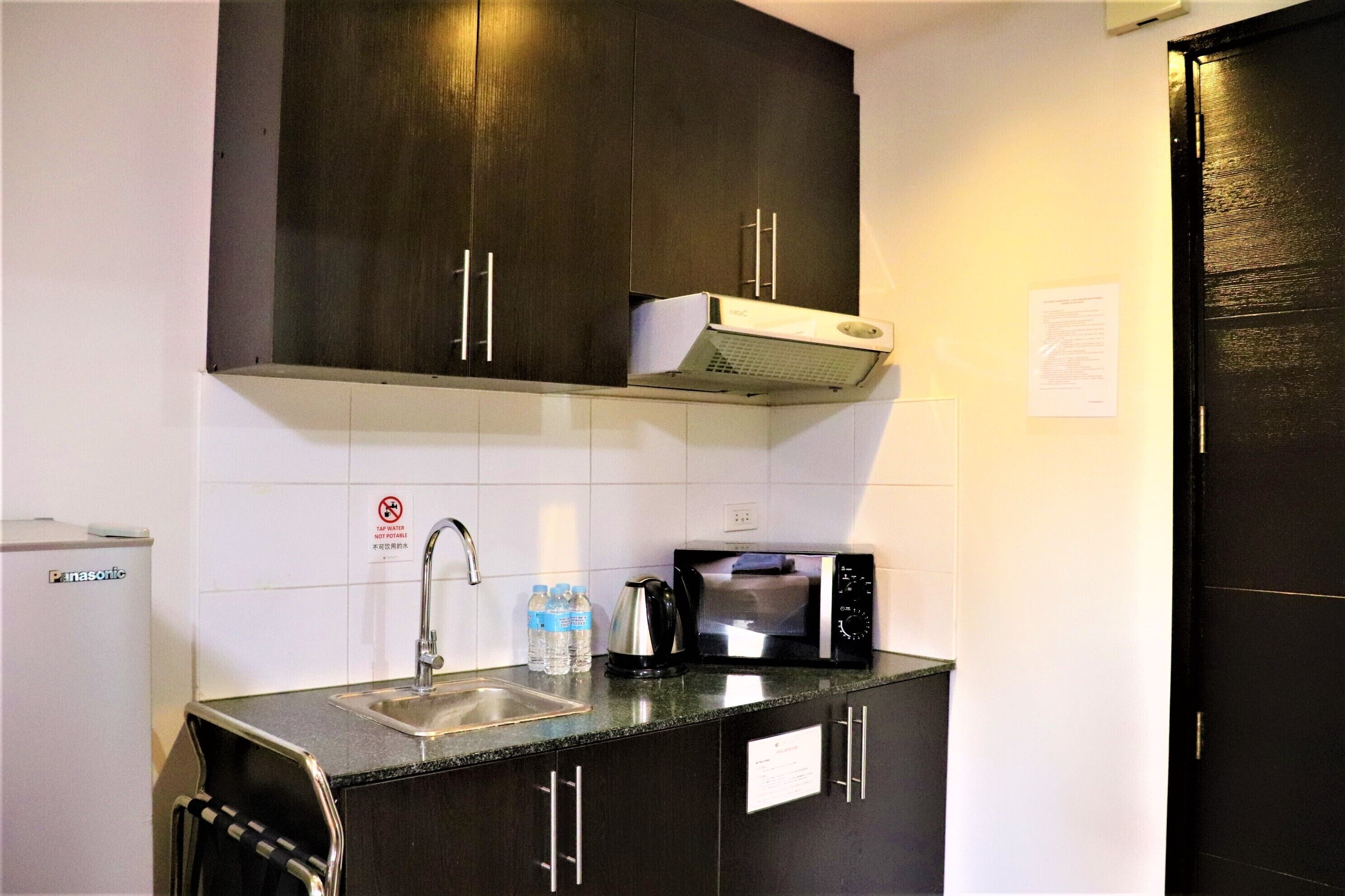 A compact kitchen with dark cabinets, a microwave, a sink, and a refrigerator.