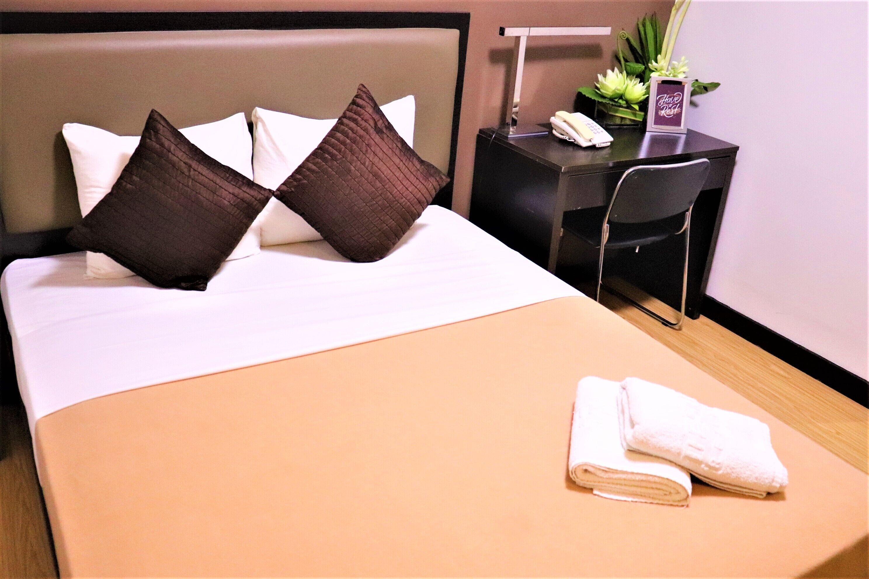 A neatly made bed with two pillows, a desk with a telephone, and a chair.
