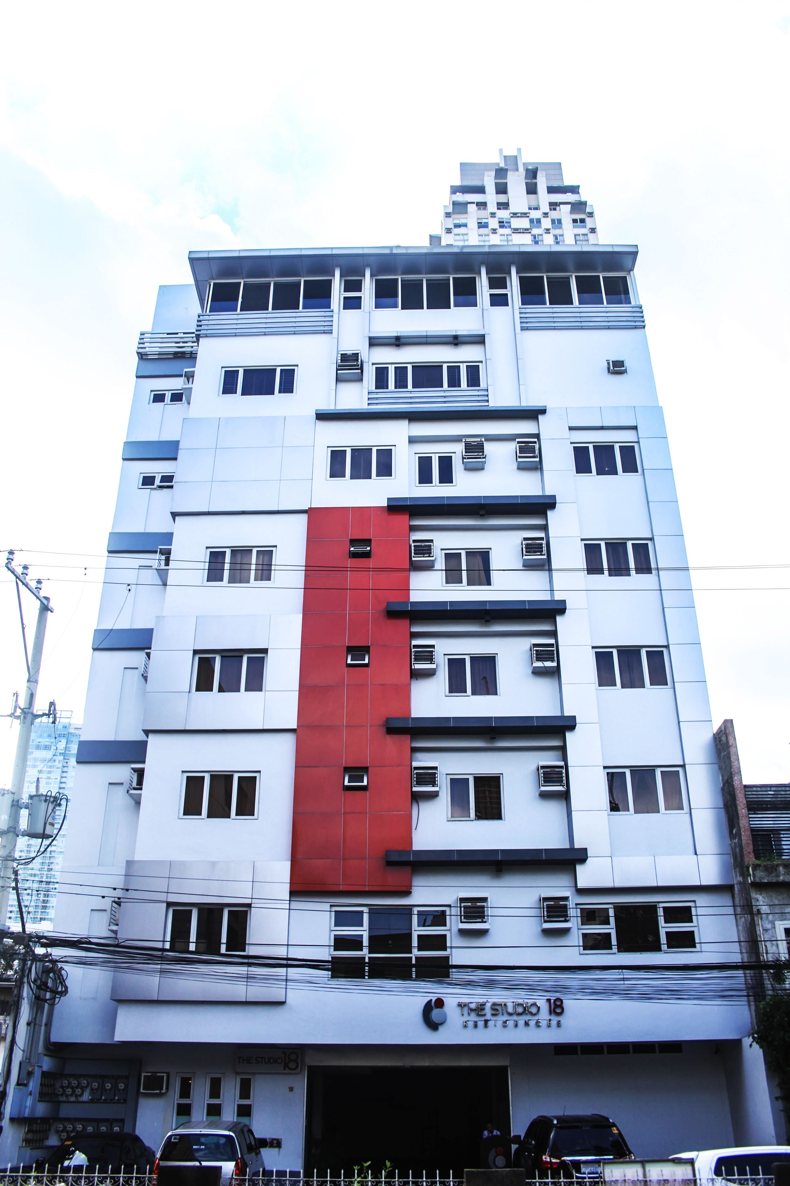 A multi-story building with a prominent red vertical stripe on the facade, multiple windows, and a sign indicating it is a studio apartment complex.