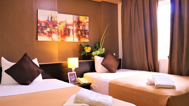 Habitación de hotel con dos camas, una mesita de noche con lámpara, un jarrón con flores y un cuadro en la pared.