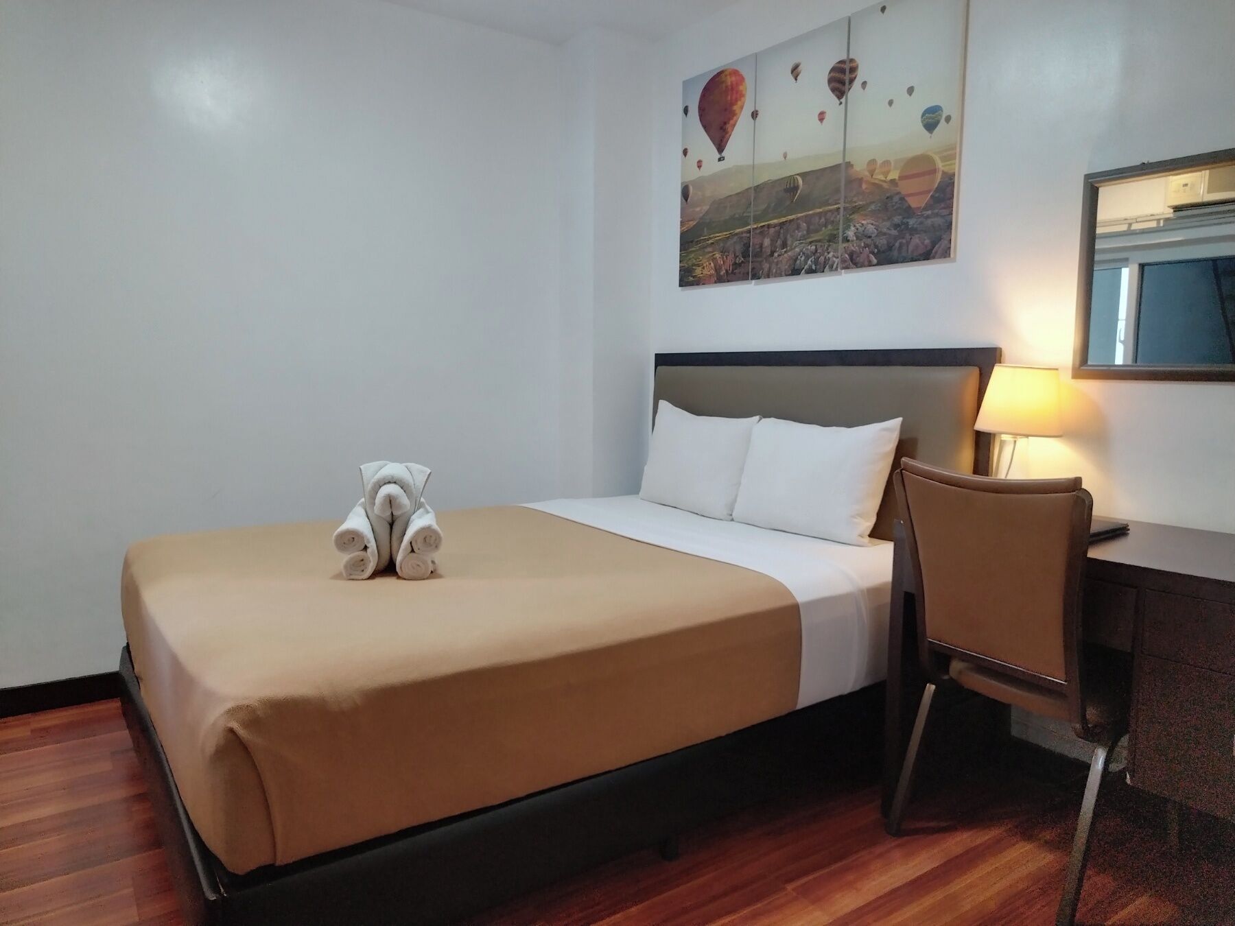 Habitación de hotel con cama, escritorio, silla y un cuadro de globos aerostáticos en la pared.