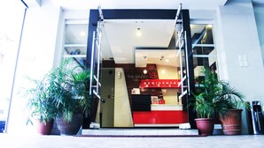Entrada de un hotel con un mostrador de recepción rojo, una escalera y plantas en macetas.