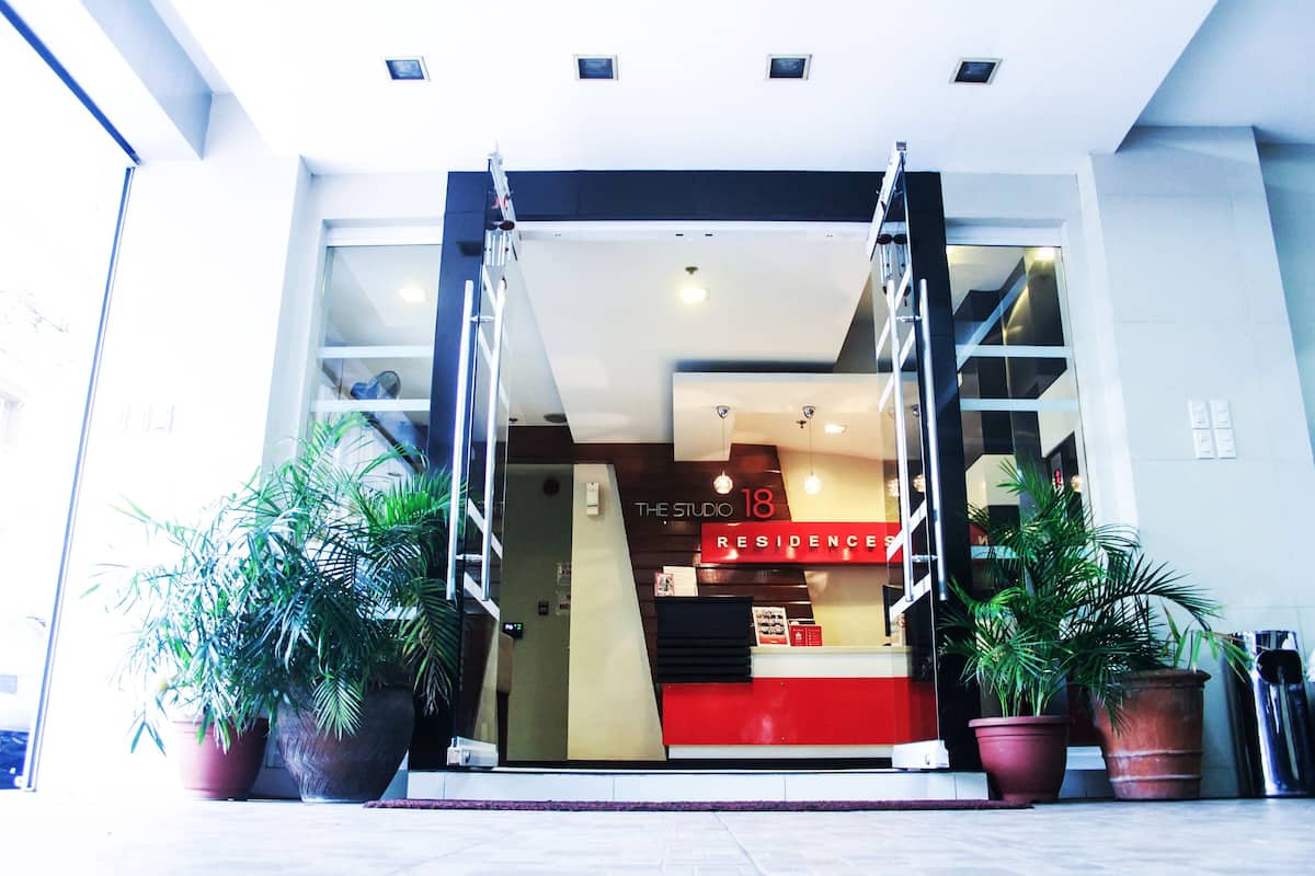 A hotel entrance with a red reception desk, a staircase, and potted plants.