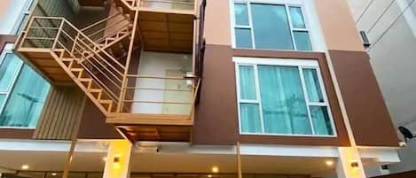 A multi-story building with a central staircase, large windows, and a parking area with cars.