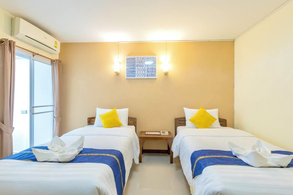 Habitación de hotel con dos camas, aire acondicionado instalado en la pared y ventana con cortinas.