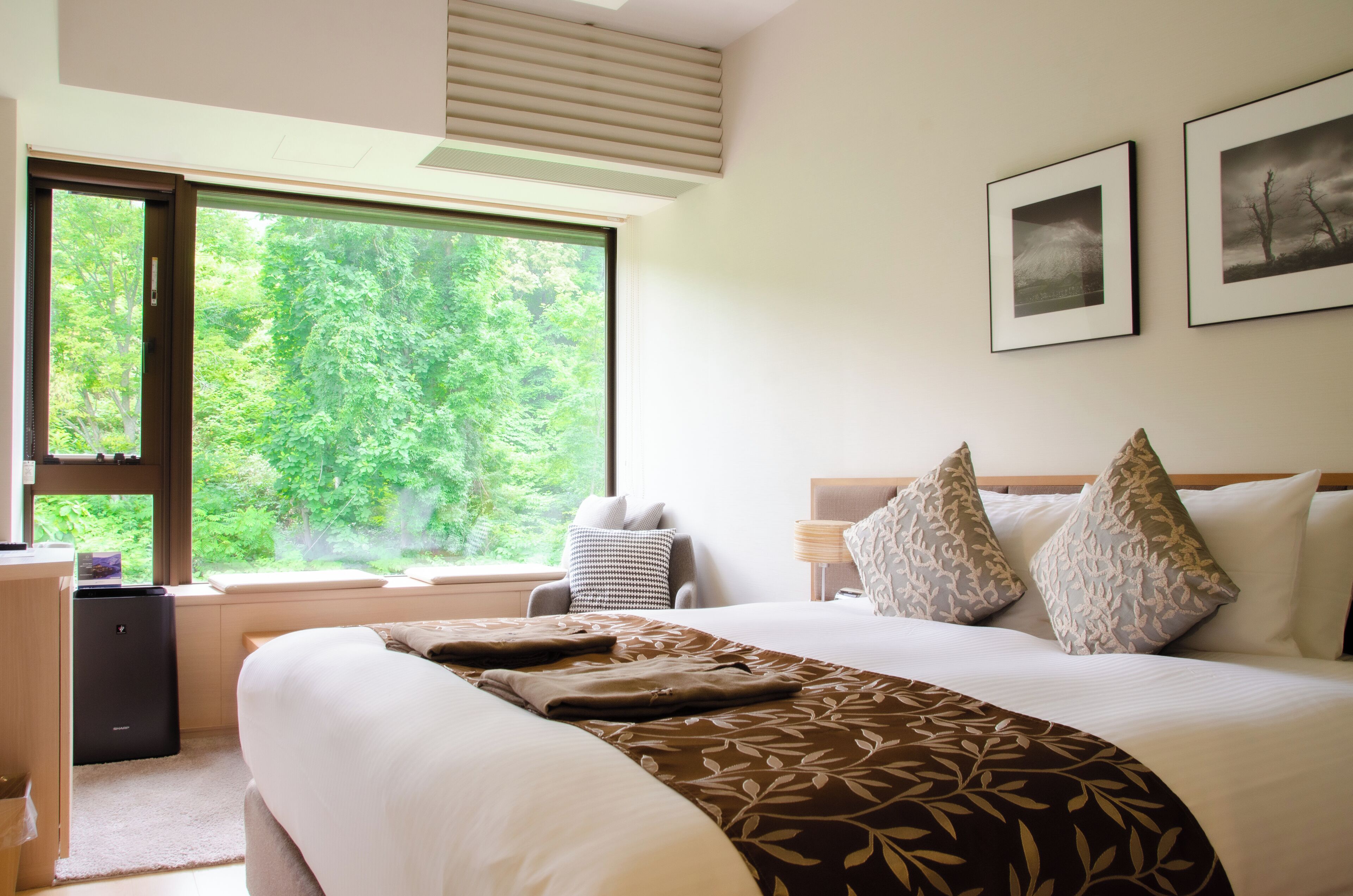A hotel room with a large bed, a desk, and a window offering a view of trees.