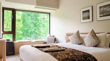 A hotel room with a large bed, a desk, and a window offering a view of trees.