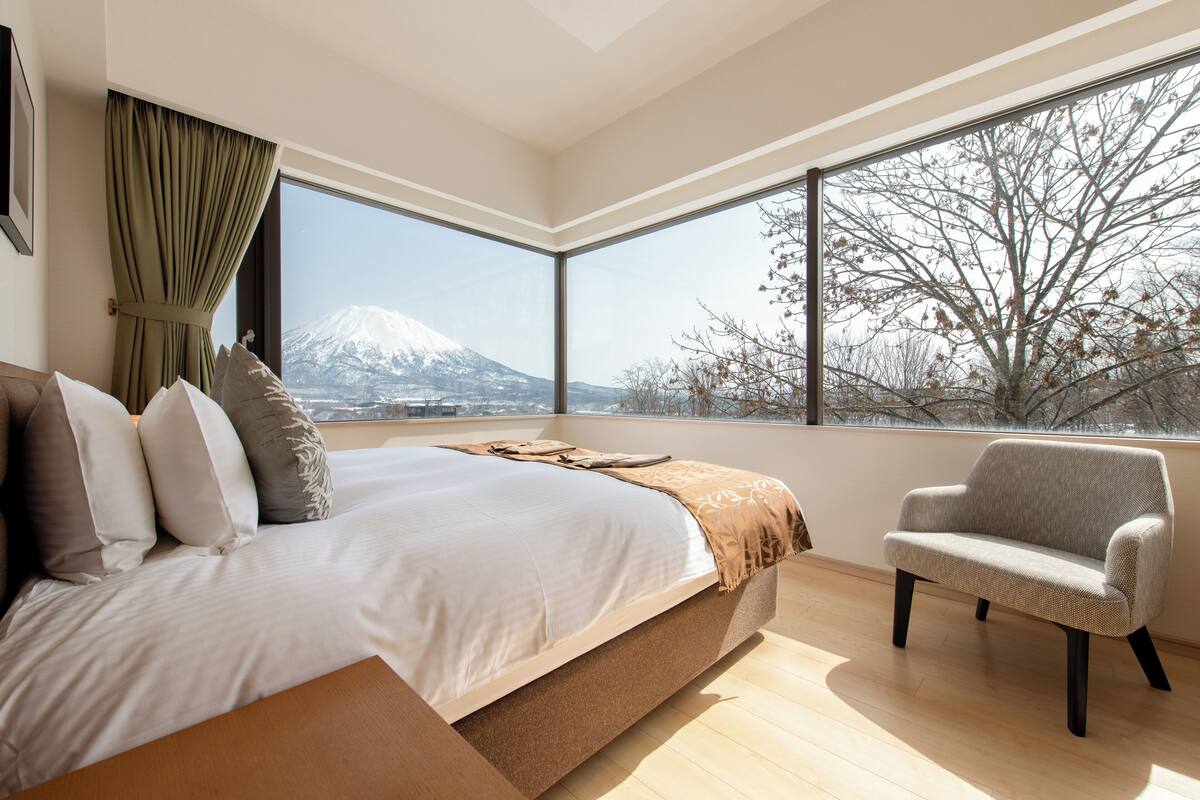 A bedroom with a large bed, a chair, and a view of a mountain.