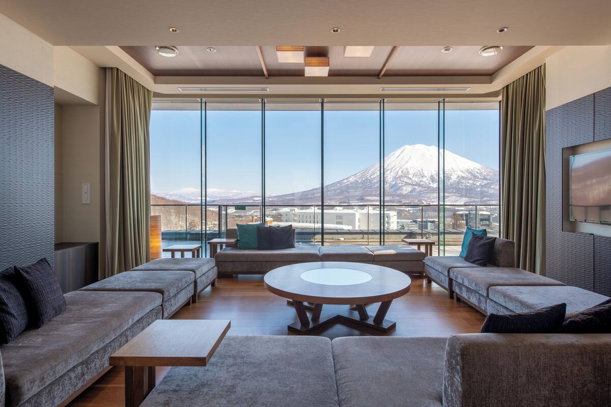 A modern living room with a large round table, sofas, and a view of a mountain.