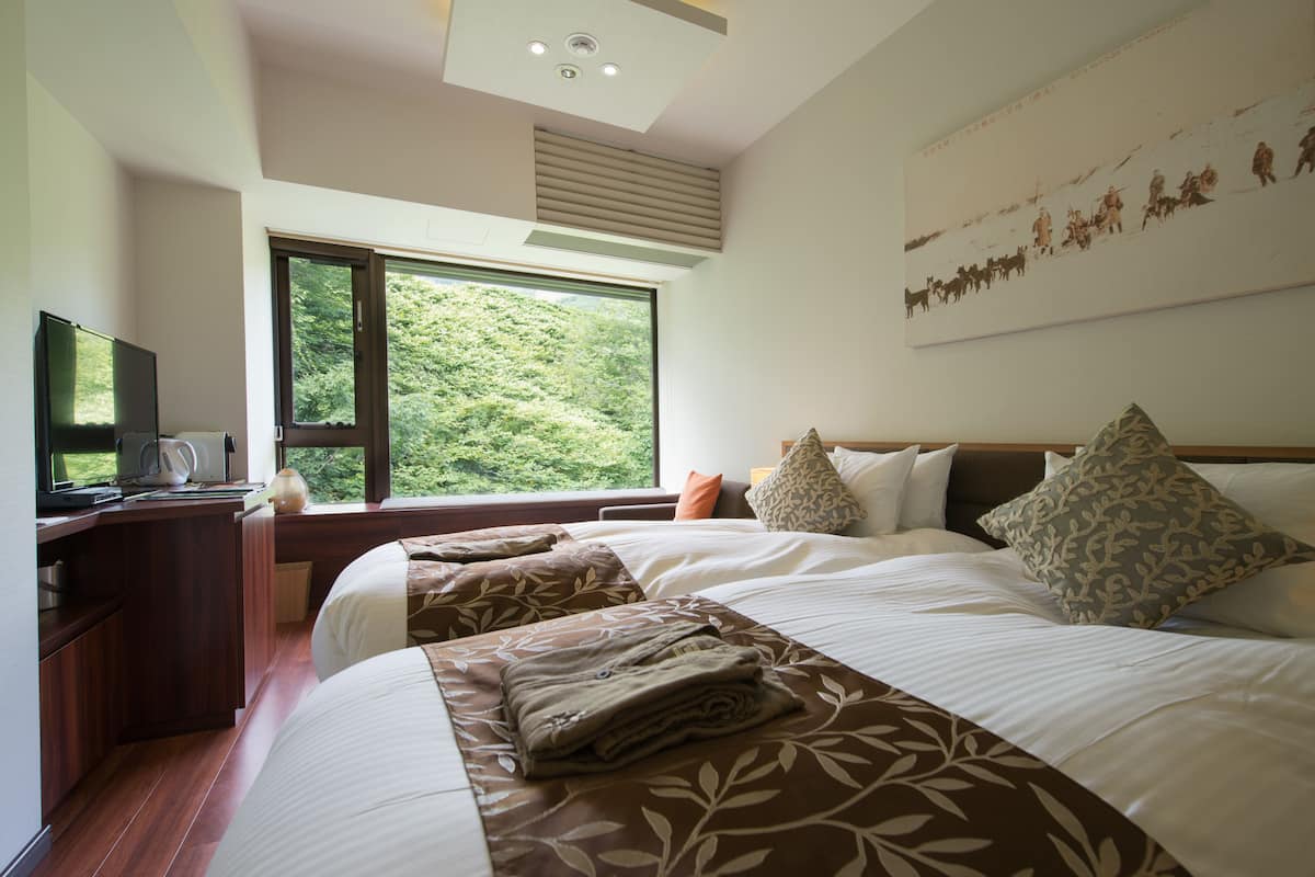 A bedroom with a large bed, a desk with a computer, and a window with a view of greenery.