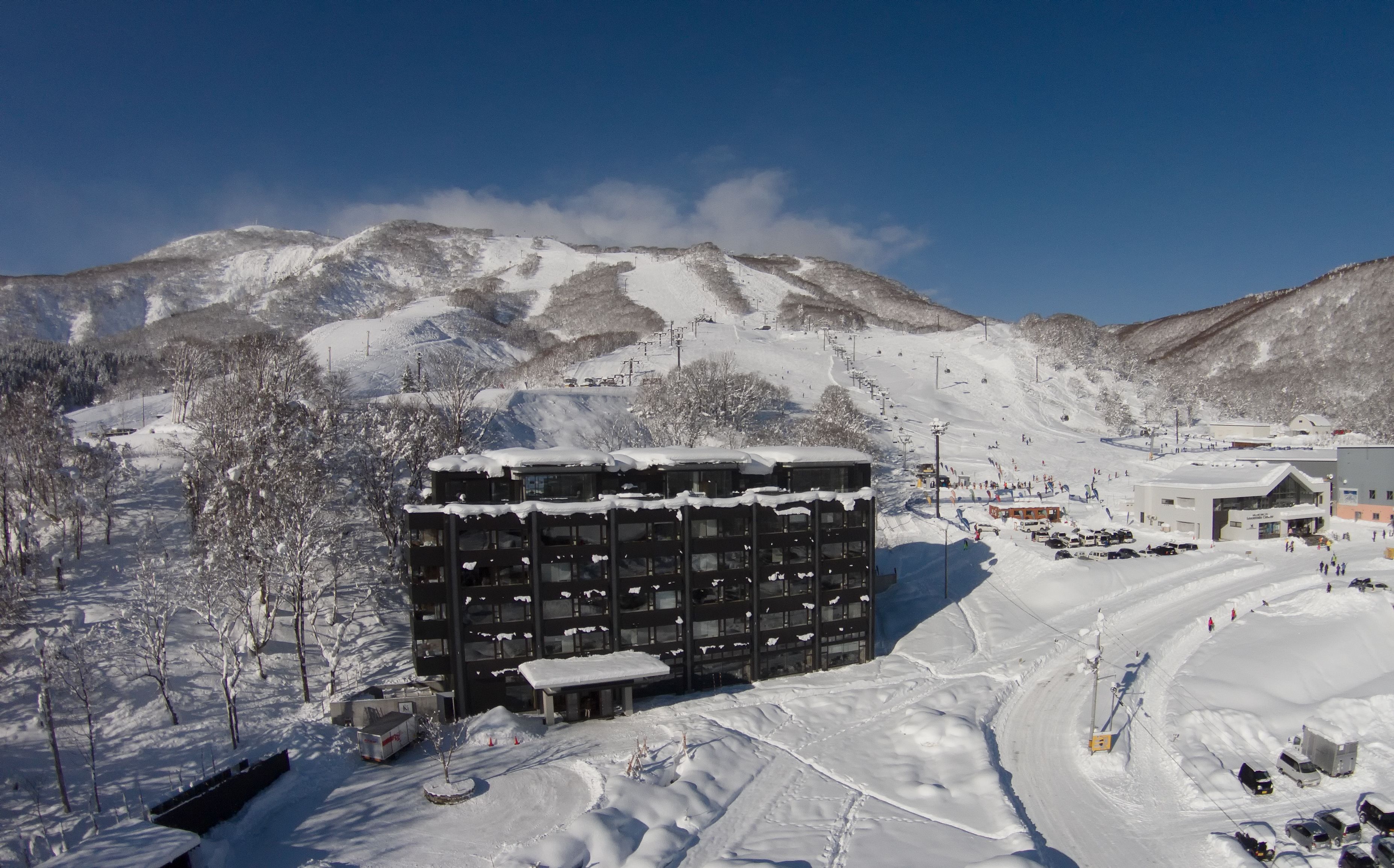 A modern building with a snow-covered roof, surrounded by a snowy landscape and mountains.
