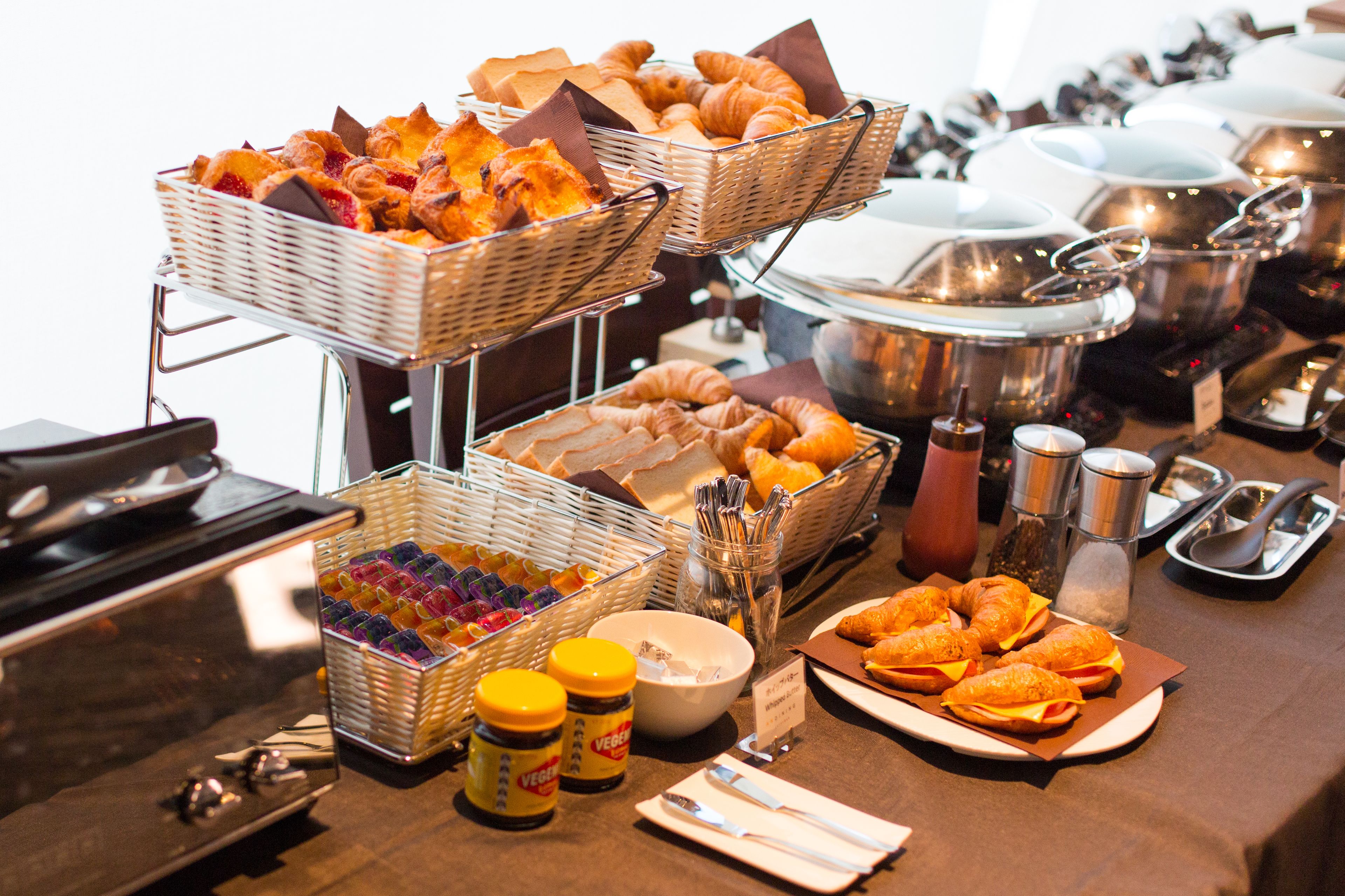 A buffet with various food items including pastries, sandwiches, and condiments.