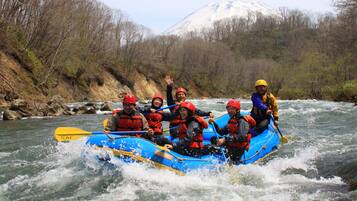 Un grupo de personas en una balsa azul navegando por un río rodeado de árboles y una montaña nevada al fondo.