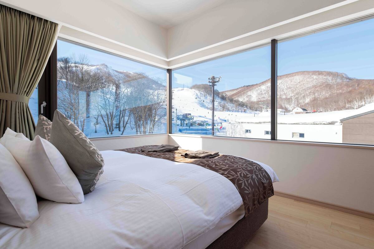 A bedroom with a large window offering a view of a snowy landscape and a ski resort.