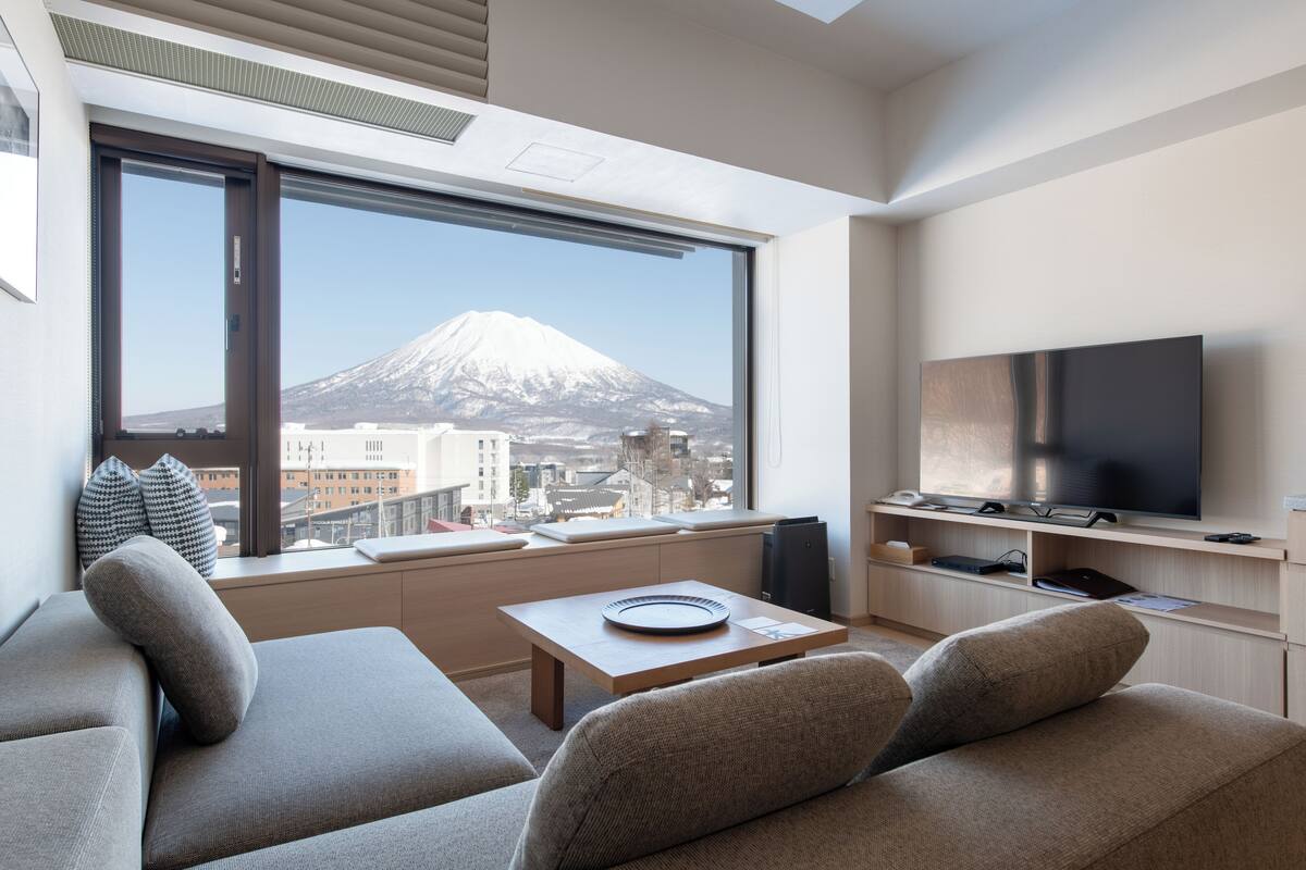 A modern living room with a large window, a flat-screen TV, and a sofa.