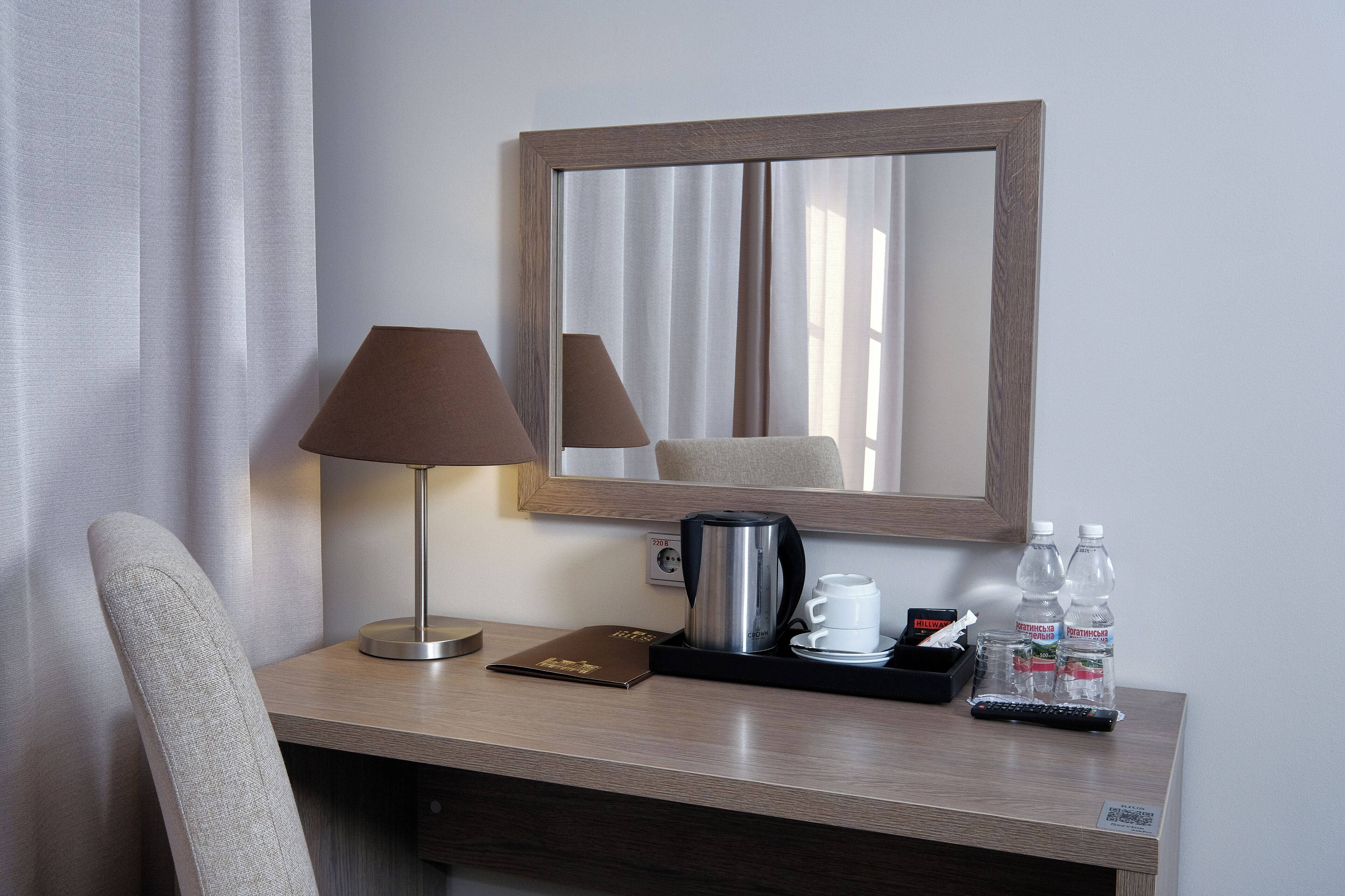 Escritorio de habitación de hotel con lámpara, cafetera, control remoto y dos botellas de agua.