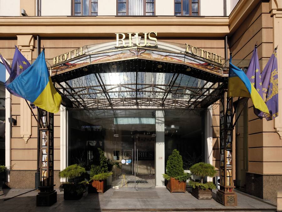 The entrance of RIUS Hotel with a glass canopy, flags, and potted plants.