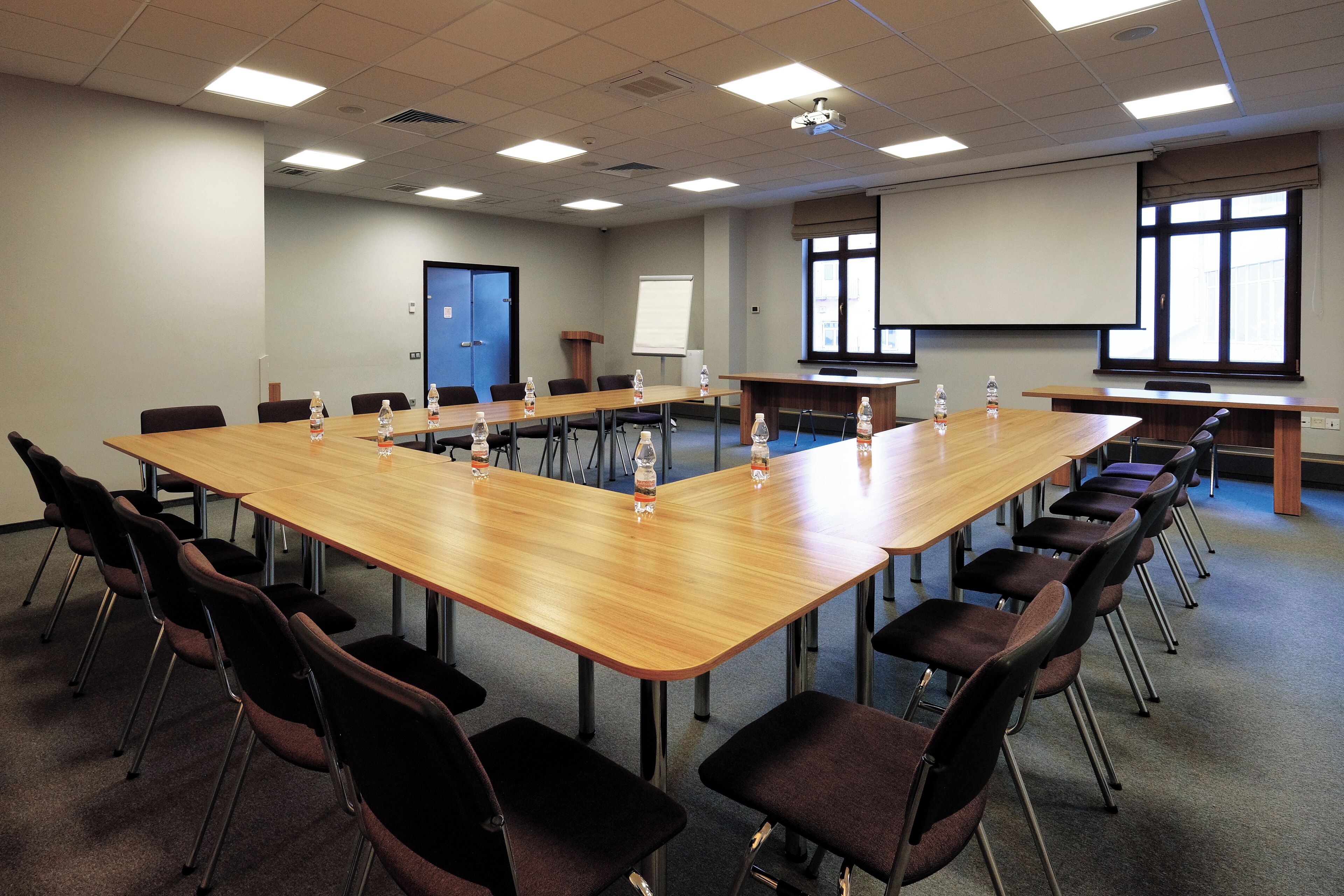 A conference room with a long table, chairs, water bottles, and a projector screen.