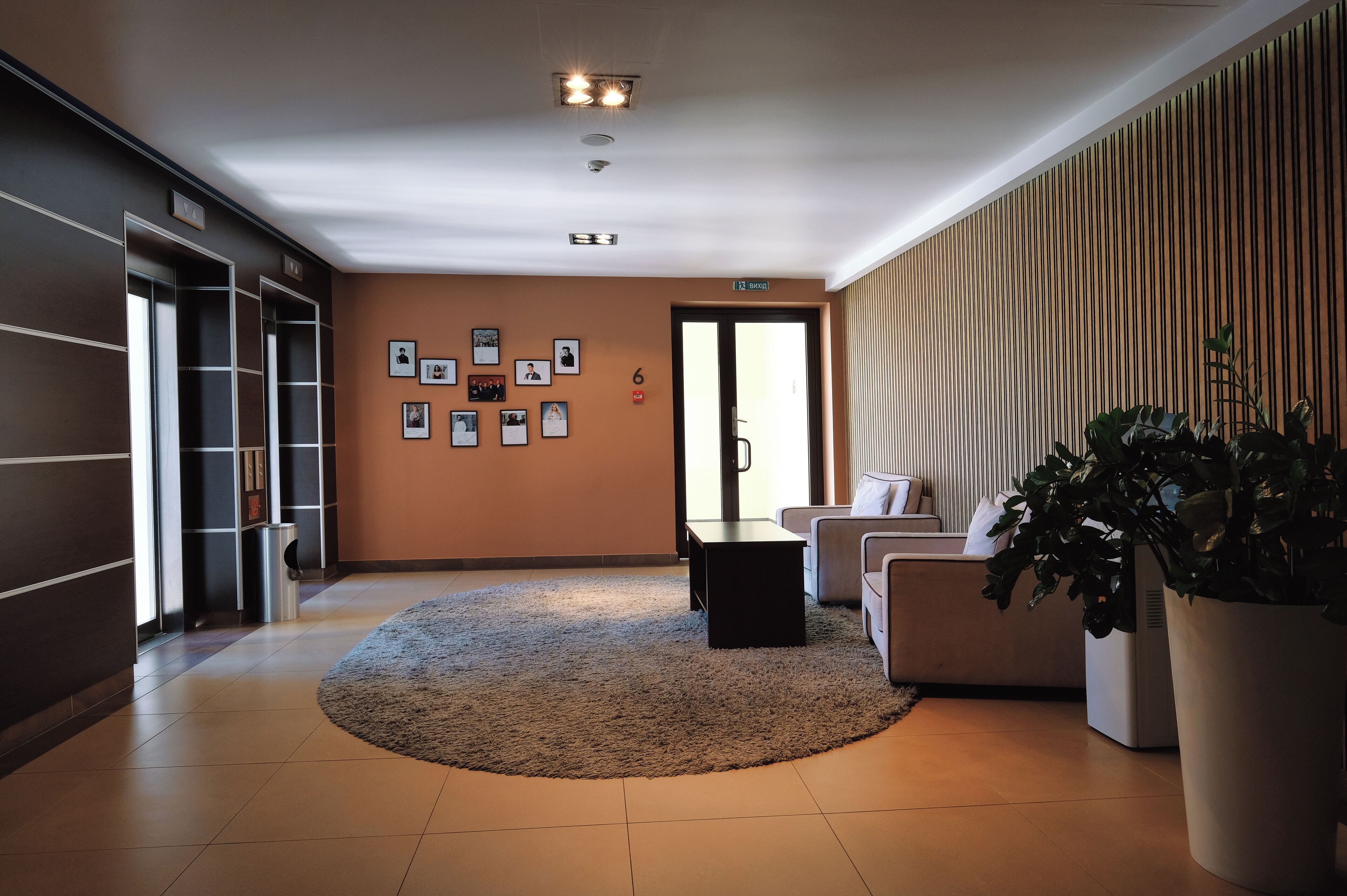 Un hall d’hôtel moderne avec un tapis rond, un coin salon comprenant un canapé et des fauteuils, une table basse et une grande plante en pot.