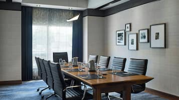 Une salle de conférence avec une longue table, six chaises, une cafetière et des tableaux encadrés accrochés au mur.